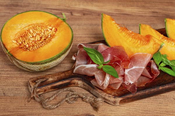 Cantaloupe melon, with prosciutto, and fresh basil, on a wooden serving board, rustic style