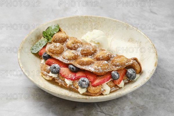 Colorful bubble waffles are served with fresh strawberries and blueberries, topped with creamy