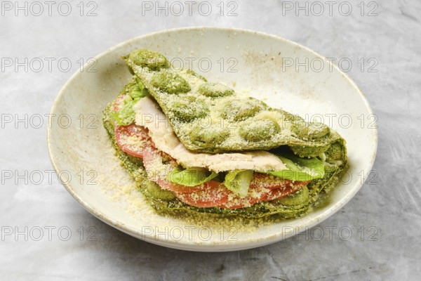 A vibrant sandwich made with green dough stacked with fresh slices of chicken, tomatoes, and