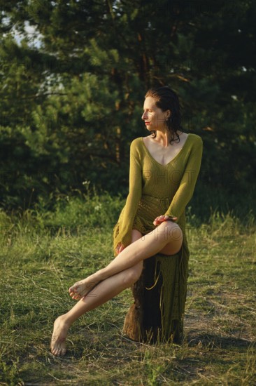 A woman enjoys a hot day by the lake, sitting gracefully on a rustic log. The sun casts a warm glow