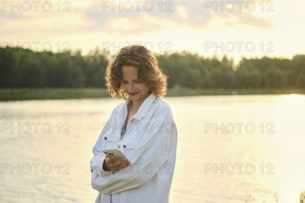 A person stands by the lake on a hot day, enjoying the sunny weather. The golden light creates a