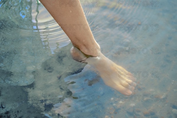 One foot dips into the refreshing lake water, creating gentle ripples on the surface. The bright