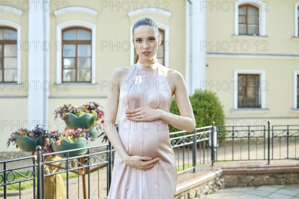A woman in a flowy dress showcases her pregnancy in a charming outdoor setting. Surrounded by a