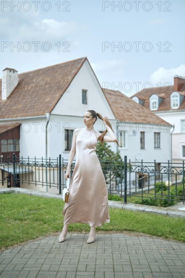 A stylish woman is posing gracefully in a lovely courtyard, dressed in a flowing pink dress. The