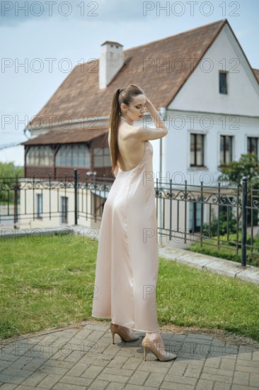 A young woman showcases her stylish outfit in a soft-colored dress while standing in a grassy area.