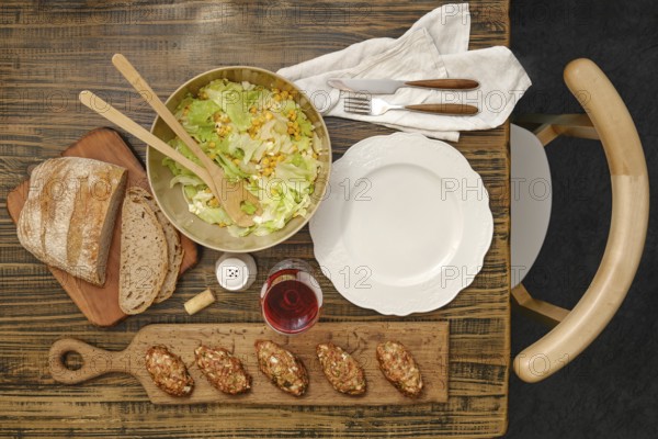 A vibrant salad with greens and corn in a bowl next to a loaf of rustic bread. Savory meat patties
