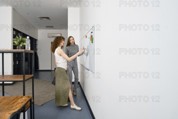 Two women actively brainstorm and discuss ideas for a women's health startup in a modern office.