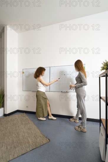 Two women engage in a brainstorming session at a contemporary office. They are standing by a