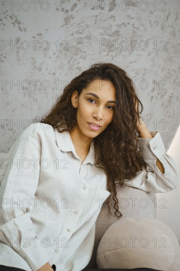 Charming woman with curly hair sits comfortably on a plush sofa in a contemporary indoor space.