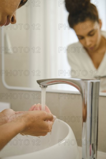 In a contemporary bathroom, a woman is washing her hands under a sleek faucet. She focuses on her