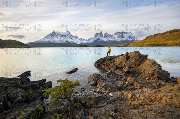 Young man on the shore of the blue lake Lago Pehoe in the evening light, Cuernos del Paine mountain