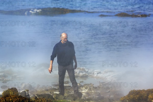 Hot spring flows into the sea, tourist on steaming rocky coast near Reykjanes, Súðavík,