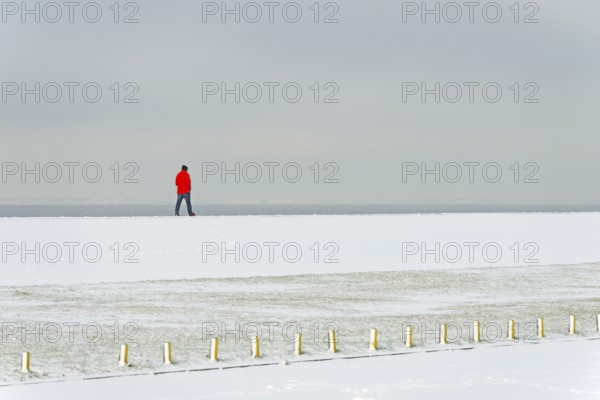Winter day, onset of winter, snow on the North Sea coast, person walking over a dyke, North Sea,