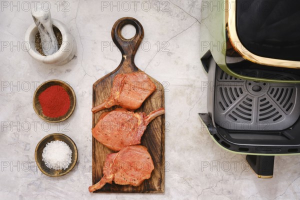Three pork rib chops are placed on a wooden cutting board, surrounded by spices including paprika