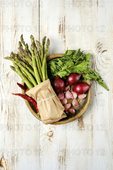 A wooden plate holds an assortment of fresh vegetables and herbs, including asparagus, red