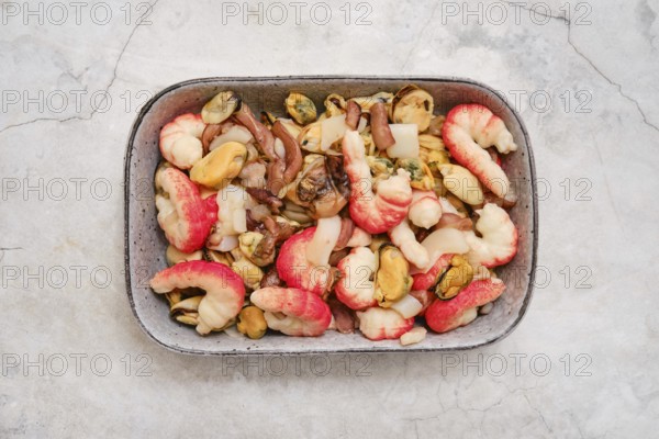 Overhead view of a bowl with shrimps, mussels, and squid. The dish showcases vibrant colors and