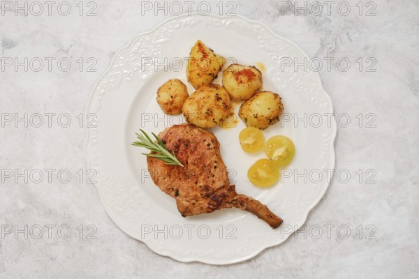 A roasted pork rib roast on a decorative white plate served with golden roasted potatoes and sweet