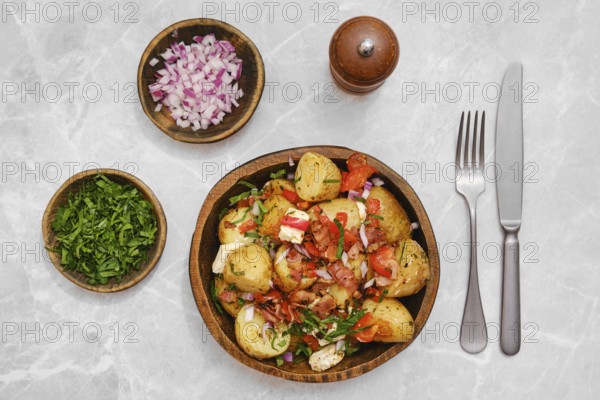 Greek potato salad in a wooden bowl, topped with tomatoes, onions, feta cheese and herbs.