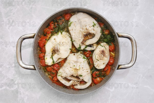Cod fish fillets are gently simmering in a tangy tomato sauce, accompanied by vibrant cherry