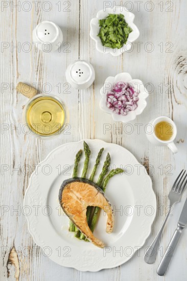 Grilled salmon and tender asparagus on a plate served for dinner. Bowls of chopped onion and herbs