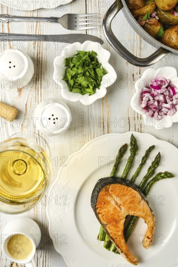 Salmon steak on a bed of asparagus, accompanied by fresh herbs and onions. A glass of white wine