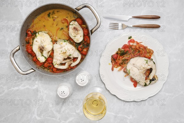 A flavorful fish dish is being prepared in a pot alongside a vibrant mix of tomatoes, carrots and