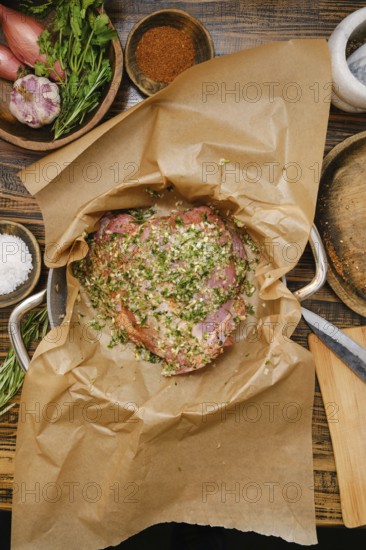 A seasoned turkey thigh in a pan lined with parchment paper, surrounded by fresh herbs, spices, and
