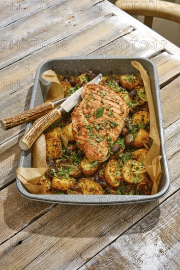 A succulent roasted turkey breast sits atop a bed of roasted golden potatoes, garnished with fresh