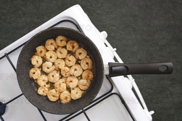 A frying pan on a stovetop filled with perfectly cooked shrimp in a kitchen. The shrimp are
