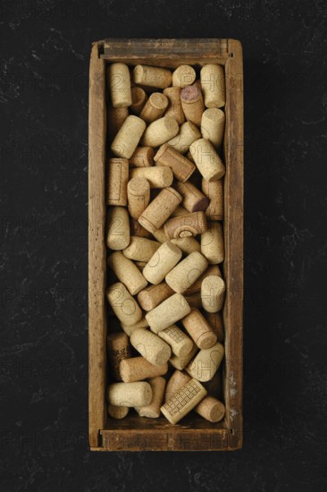 A wooden box is filled with an assortment of wine corks, showcasing various shapes and textures