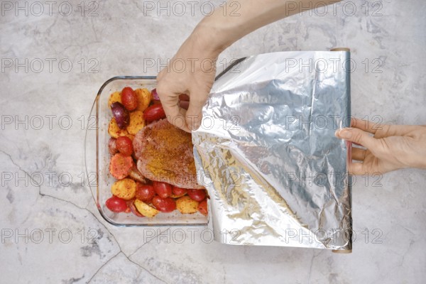 A hand gently covers a baking dish filled with seasoned turkey breast and juicy vegetables with