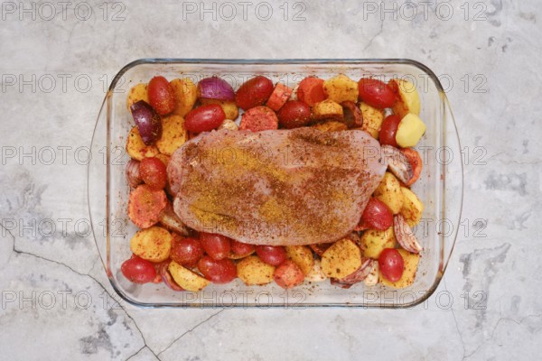 A perfectly seasoned turkey breast rests on a bed of vibrant potatoes, tomatoes and onion ready to