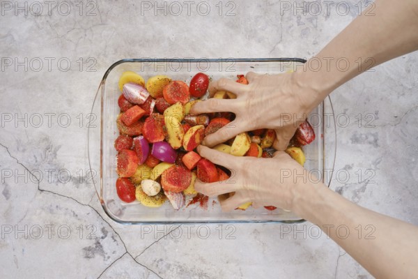 Hands mix together seasoned potatoes, tomatoes, and onions in a glass dish for a turkey breast