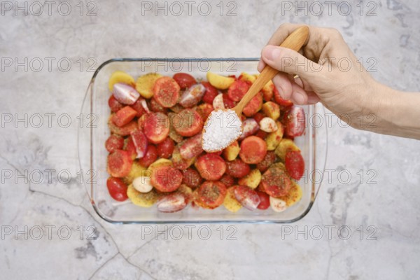 A hand sprinkles salt over colorful fresh vegetables and seasonings, preparing a vibrant mix to