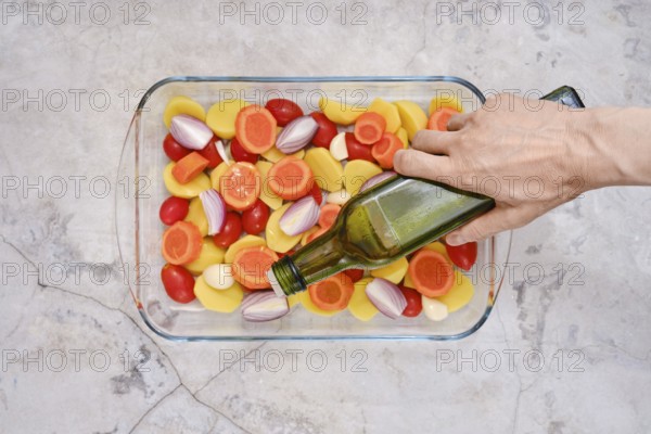 Pouring olive oil on slices of fresh vegetables including tomatoes, carrots, potatoes and onions