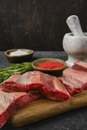 A selection of raw beef ribs is arranged on a wooden cutting board alongside bowls of seasoning.