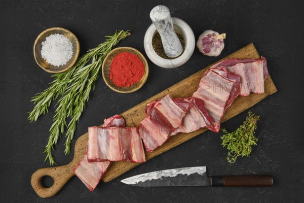 Fresh raw beef short ribs lay on a wooden cutting board alongside bowls of seasoning, herbs, and a