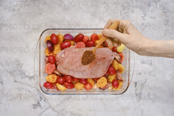 A hand sprinkles a blend of spices over a raw turkey breast resting on a bed of vibrant red and
