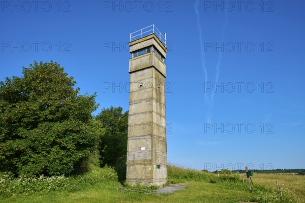 Isolated watchtower of the former inner German border under a cloudless sky next to a green