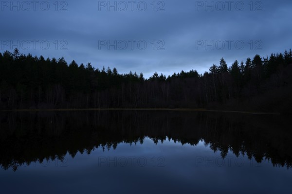 A quiet night scene with dark forest and reflection in the still water of a lake, Mülbenersee,