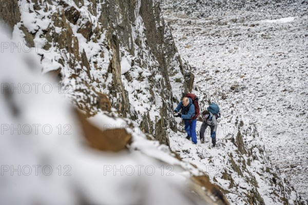 Mountaineer on a rope-secured path in a steep, rocky mountain landscape with fresh snow in summer,