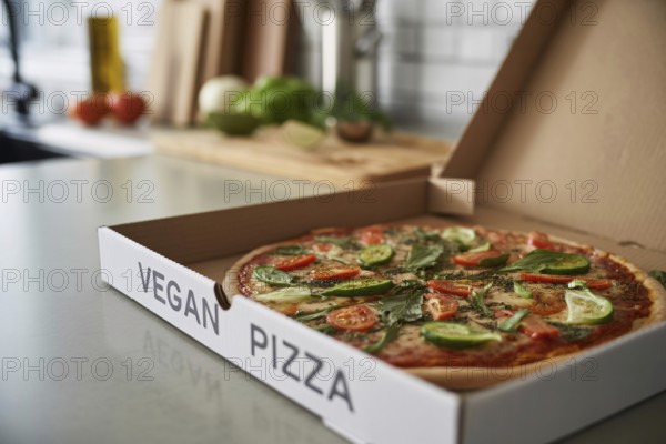 Freshly delivered vegetable pizza in box labeled vegan pizza on kitchen counter. Healthy