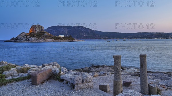 Ruins in the foreground and a calm sea with a rocky island at dusk, Agios Stefanos Beach, Agios