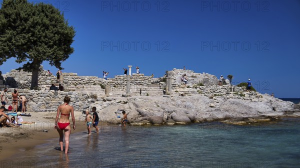 People exploring ancient ruins on the beach under a clear blue sky, Agios Stefanos Beach, Agios