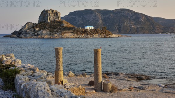 Ancient columns in front of the sea in warm evening light with an island in the background, Agios