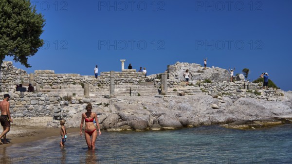 Families enjoy the day at ancient ruins by the sea with clear skies, Agios Stefanos Beach, Agios