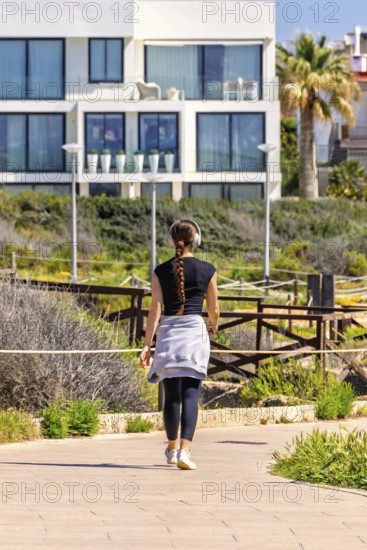 Young woman walking outdoors on a footpath in a residential area and listening to music with