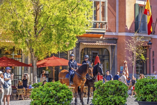 Mounted police officers sitting on horses in a town square with restaurants and people in the old