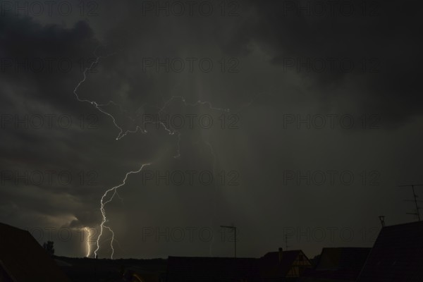 Dark clouds gather as lightning strikes light up the night above the rooftops. The intense storm