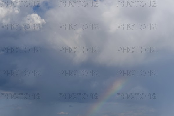 Bright sunlight breaks through large clouds after a rain shower and reveals a magnificent rainbow